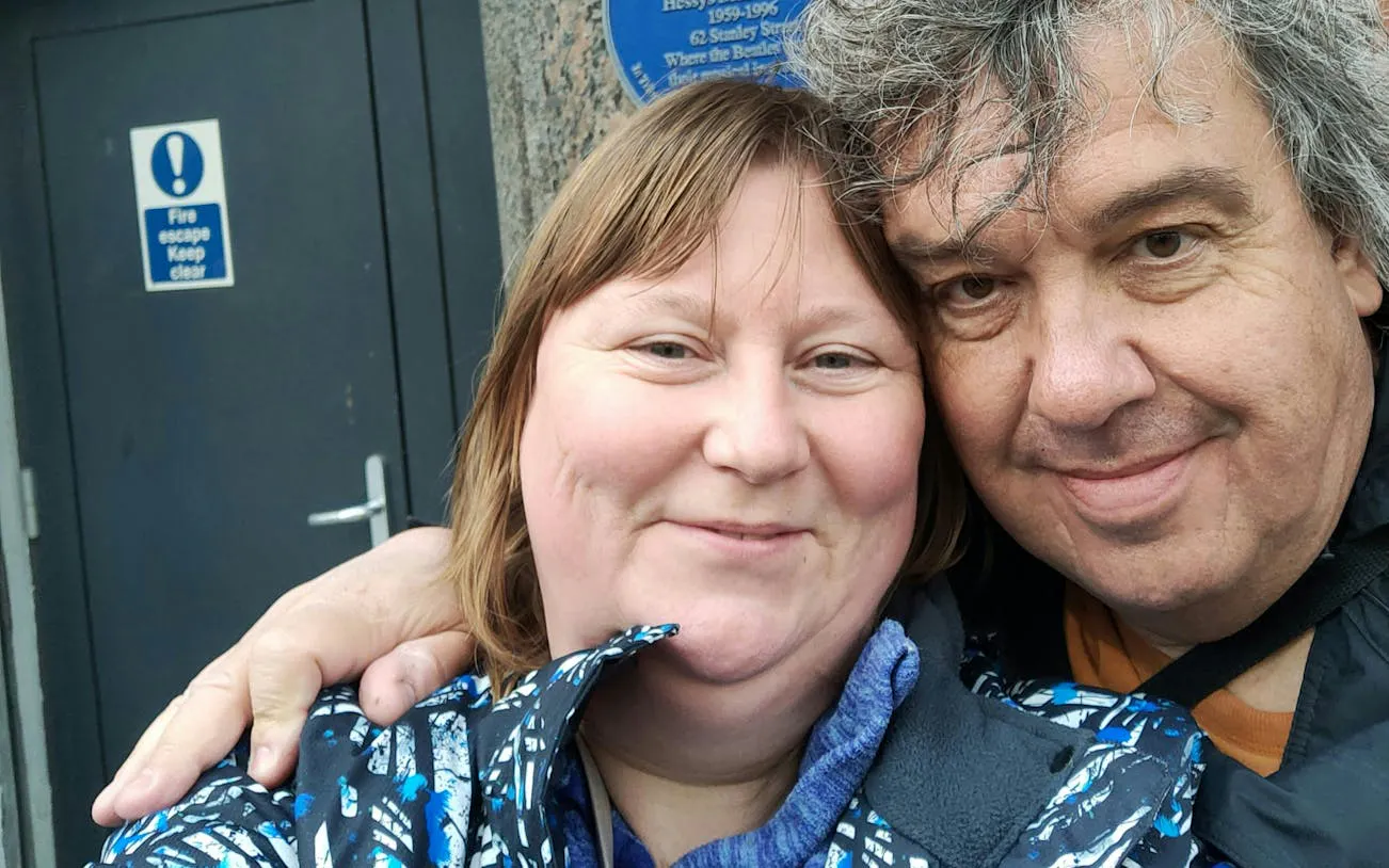Couple smiling in front of a blue plaque on Liverpool's Rock 'n' Roll Legends tour.