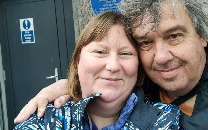 Couple smiling in front of a blue plaque on Liverpool's Rock 'n' Roll Legends tour.