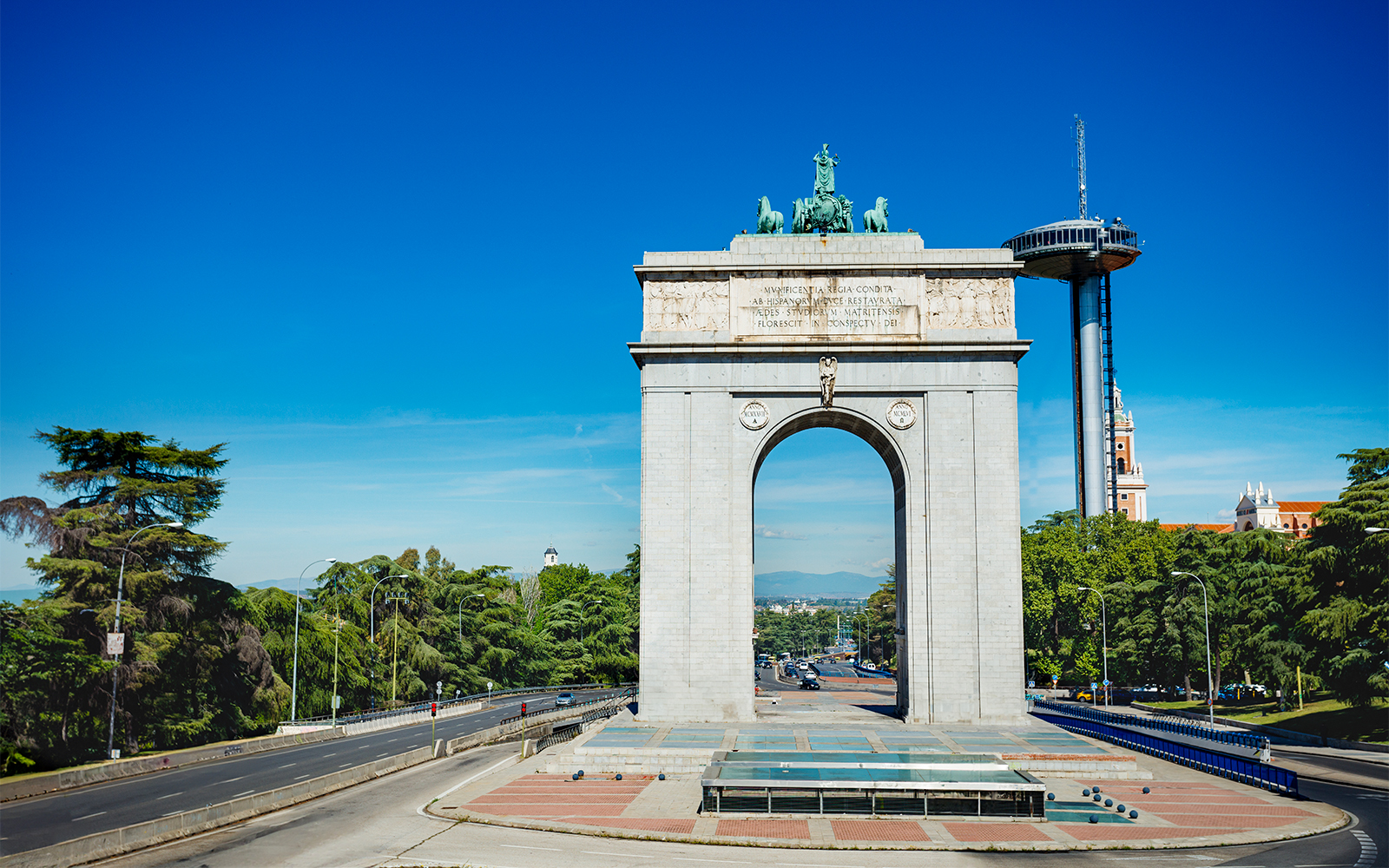 Victory Arch in Moncloa, Madrid with surrounding trees and clear sky.