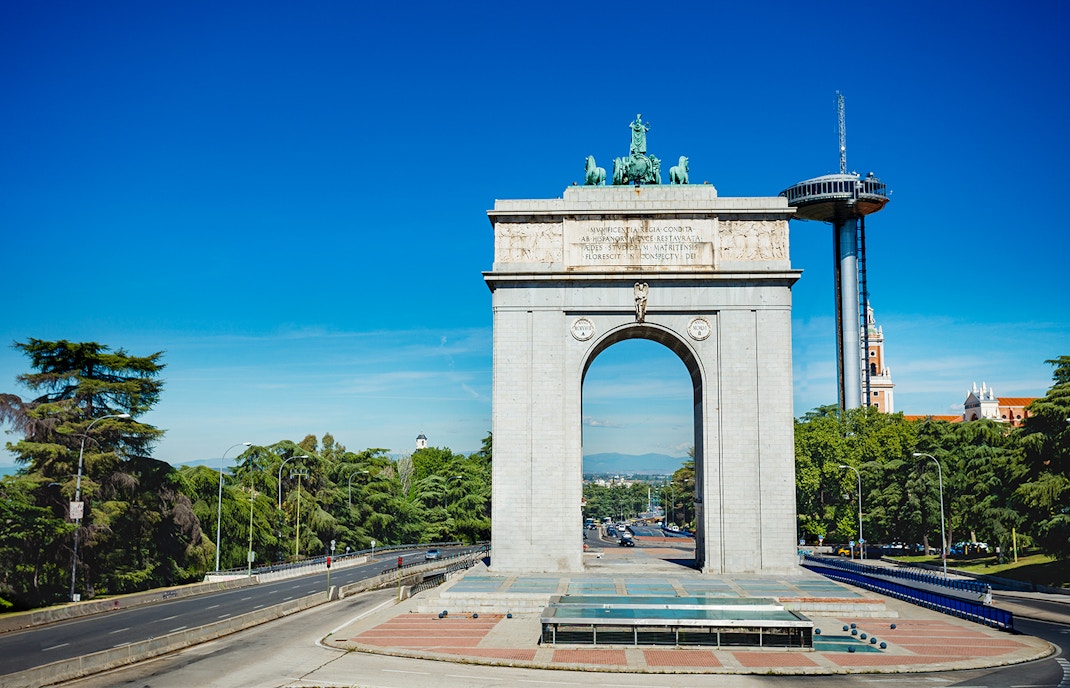 Victory Arch in Moncloa, Madrid with surrounding trees and clear sky.