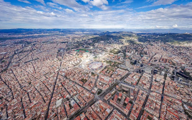 Aerial view of Barcelona cityscape with mountains in the background.