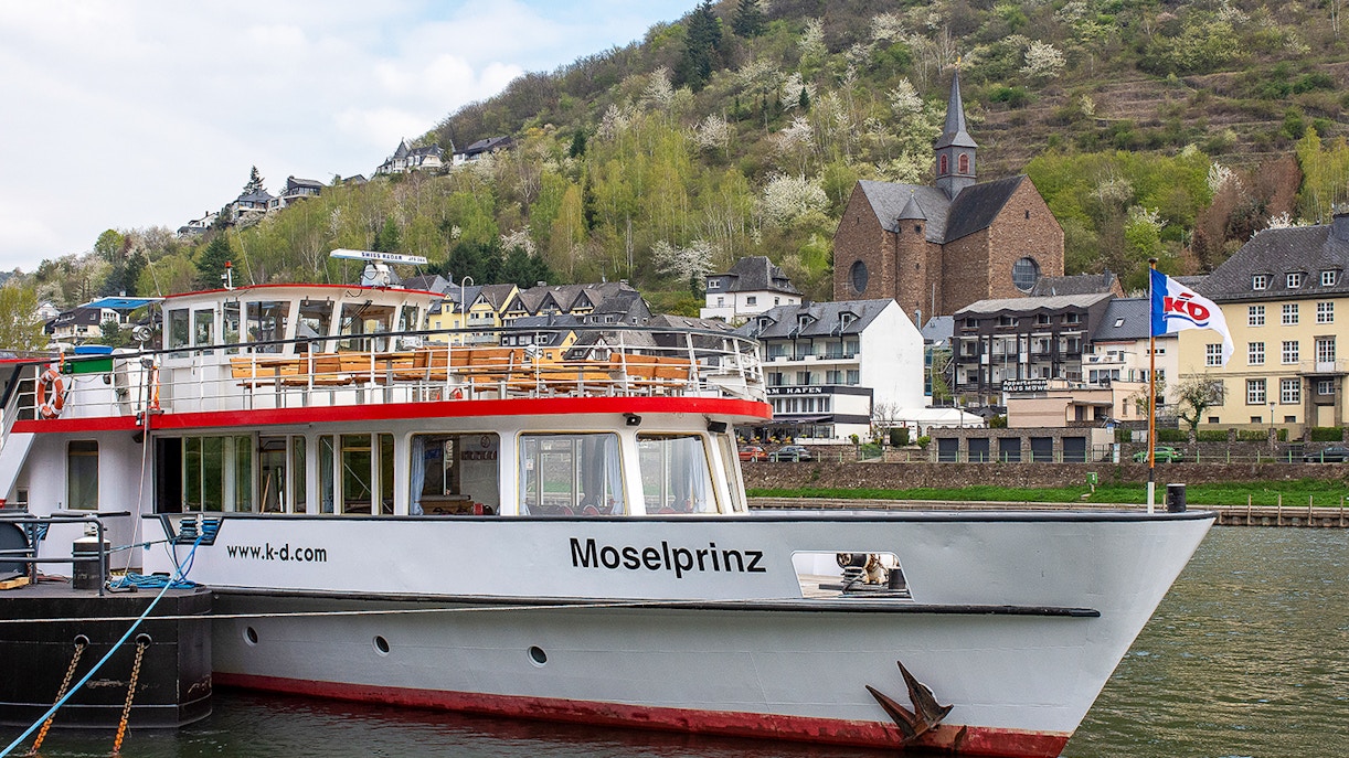 Cruise ship Moselprinz docked in Cochem with hillside and church in background.