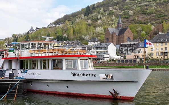 Cruise ship Moselprinz docked in Cochem with hillside and church in background.