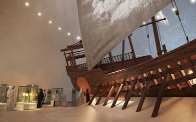 Visitors viewing maritime exhibits at Zayed National Museum, featuring a large traditional wooden ship.