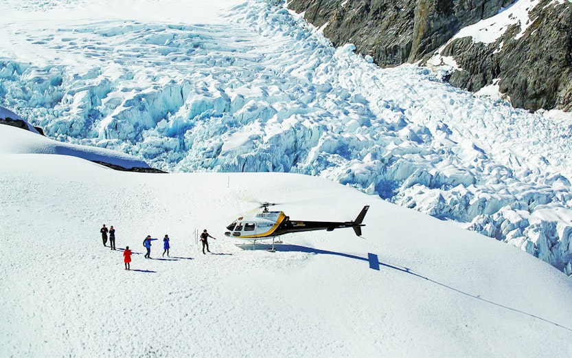 Helicopter landing on Franz Josef Glacier with hikers preparing for a guided tour.