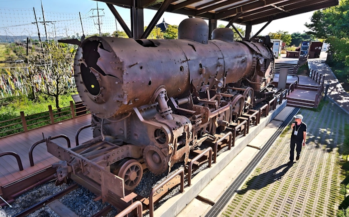 Rusty steam locomotive at DMZ, South Korea, with barbed wire fence in background.