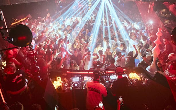 DJ performing at Club Chinois, Ibiza with crowd dancing under vibrant lights.