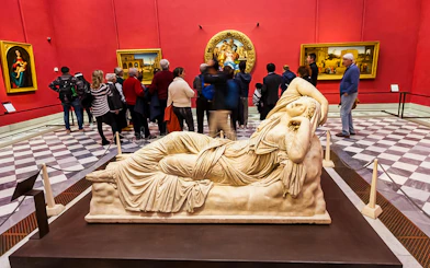 Reclining marble sculpture in Uffizi Gallery with visitors in red-walled room.