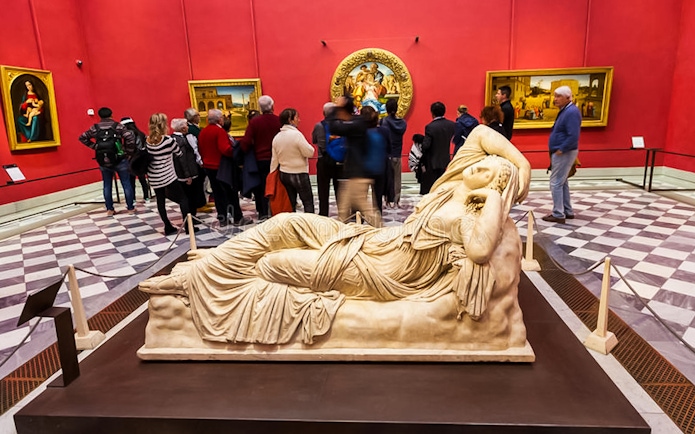 Reclining marble sculpture in Uffizi Gallery with visitors in red-walled room.