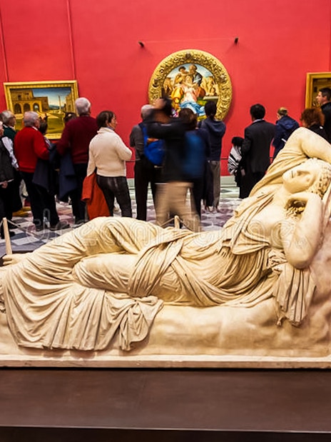 Reclining marble sculpture in Uffizi Gallery with visitors in red-walled room.