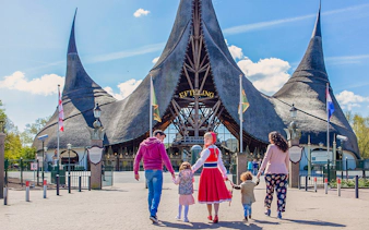 Family walking towards Efteling Theme Park entrance with iconic thatched roof.