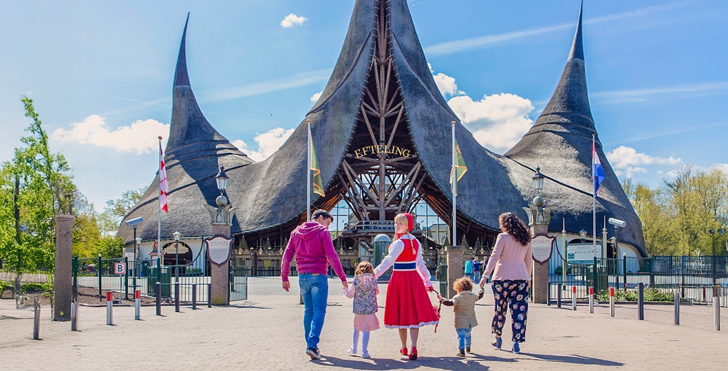 Family walking towards Efteling Theme Park entrance with iconic thatched roof.