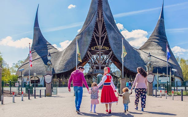 Family walking towards Efteling Theme Park entrance with iconic thatched roof.
