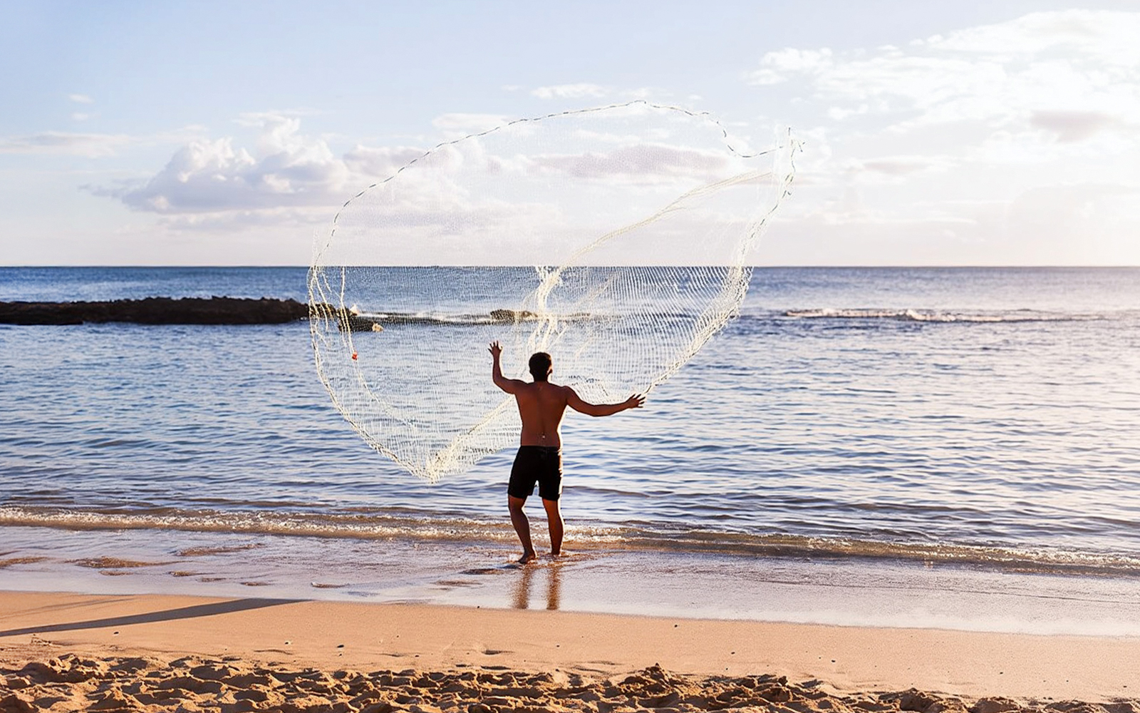 Man casting fishing net at Paradise Cove Luau beach, Hawaii.