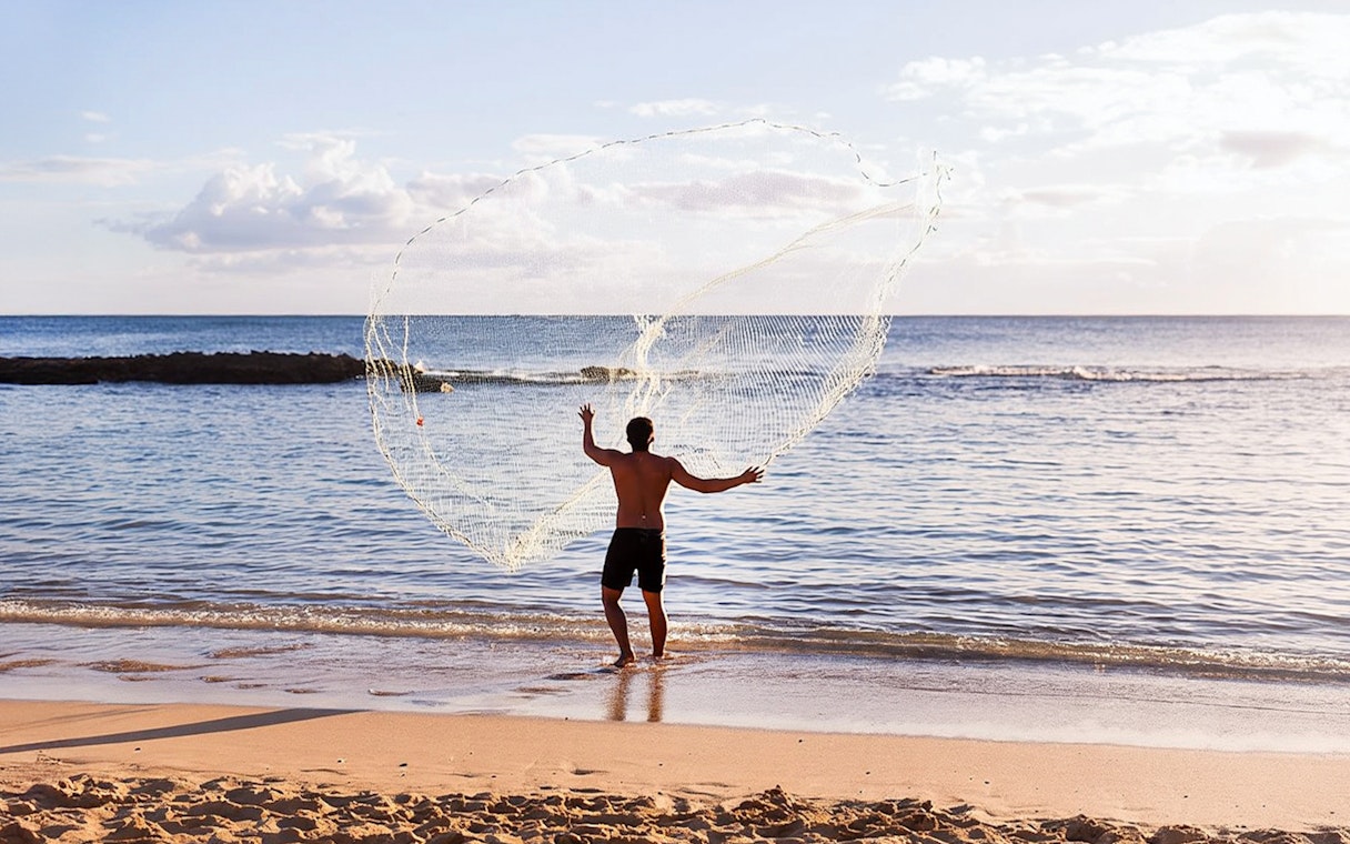 Man casting fishing net at Paradise Cove Luau beach, Hawaii.