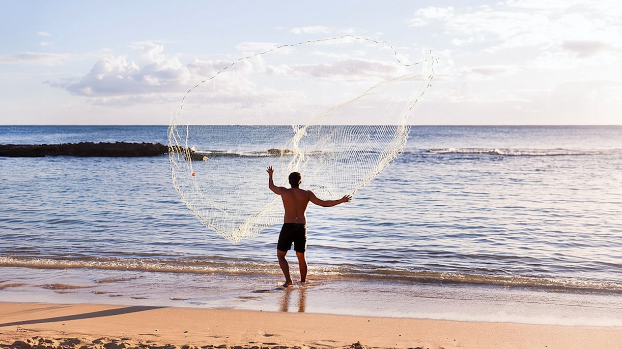 Man casting fishing net at Paradise Cove Luau beach, Hawaii.