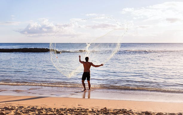 Man casting fishing net at Paradise Cove Luau beach, Hawaii.