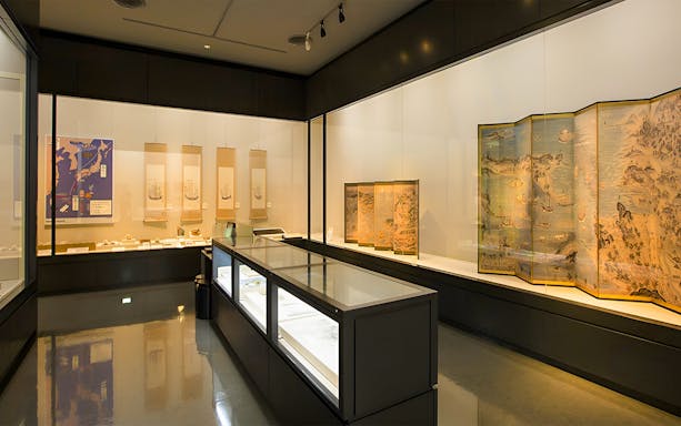Exhibit room at Okinawa Prefectural Museum displaying historical maps and artifacts.