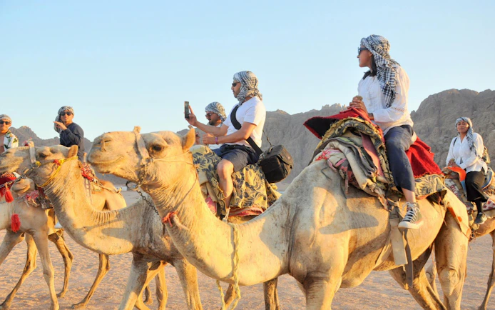 Camel ride along the Souss River in Agadir with tourists capturing the experience.