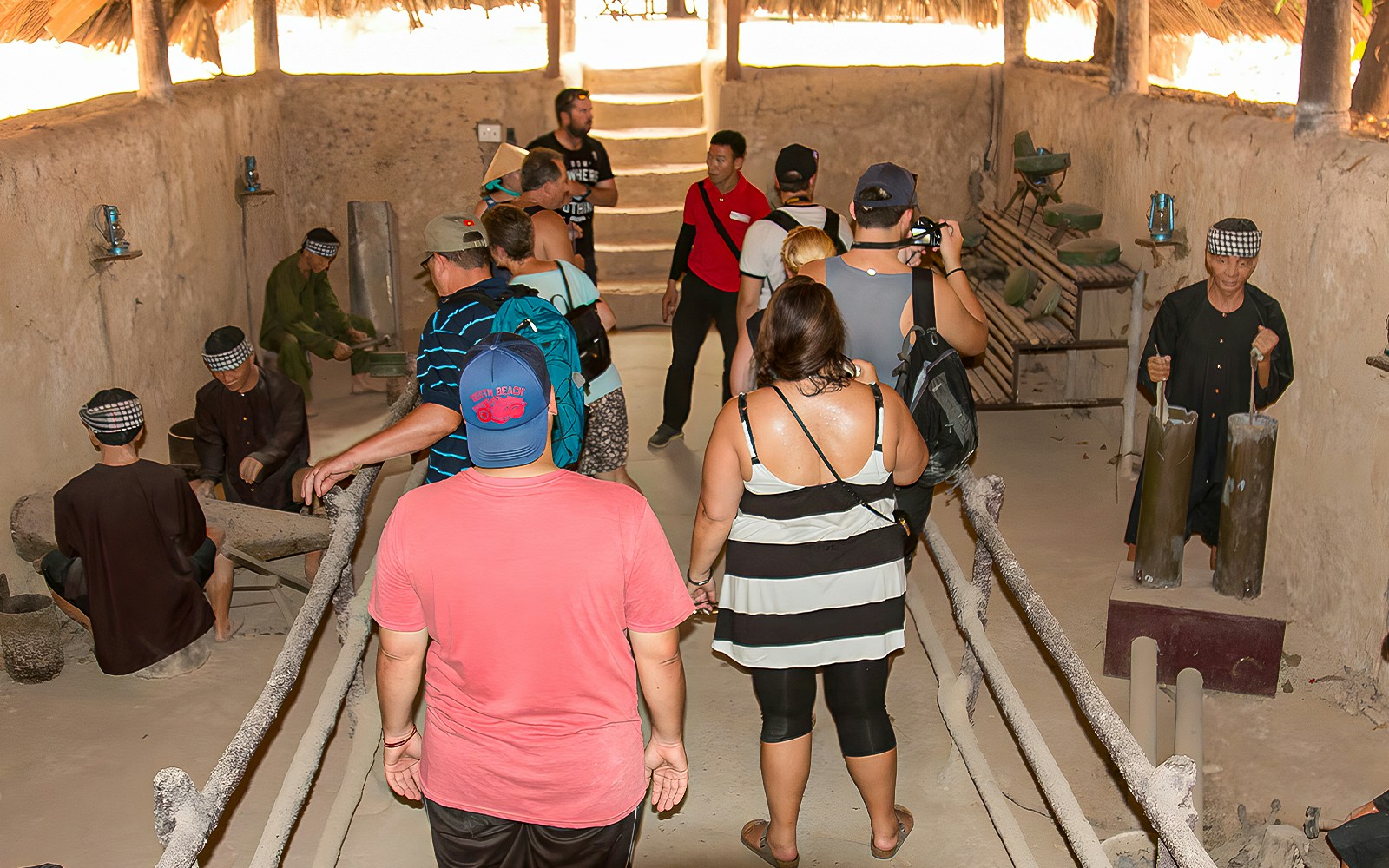 Tour group with guide in Cu Chi tunnel kitchen, observing traditional cooking methods.