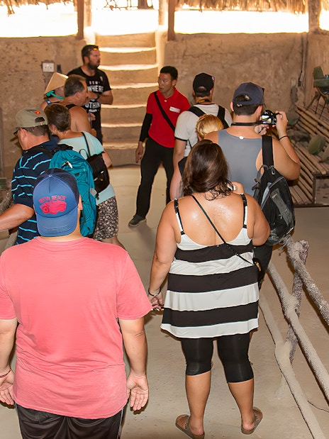Tour group with guide in Cu Chi tunnel kitchen, observing traditional cooking methods.