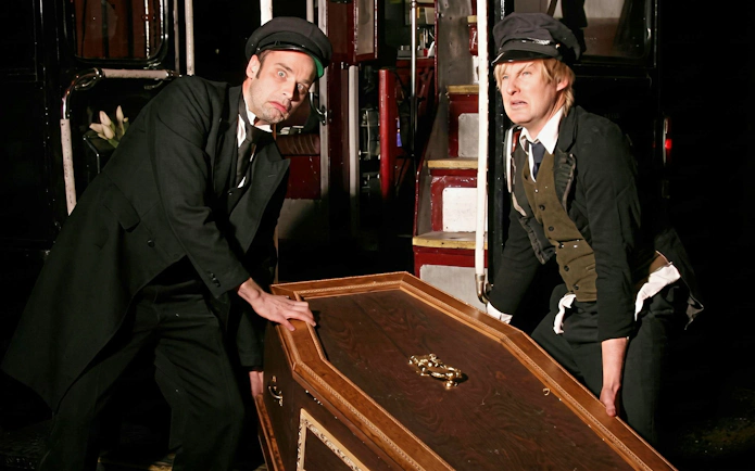 Two actors in vintage attire lifting a coffin on a ghost tour bus.
