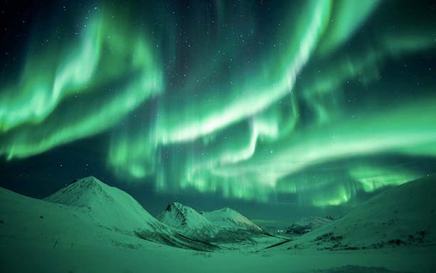 Northern lights illuminating snowy mountains near Tromsø, Norway.