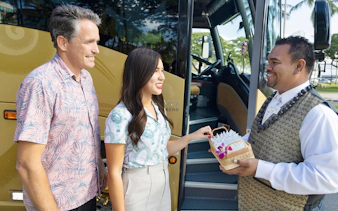 Driver welcoming passengers with leis before boarding Royal Star tour bus.