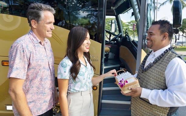 Driver welcoming passengers with leis before boarding Royal Star tour bus.