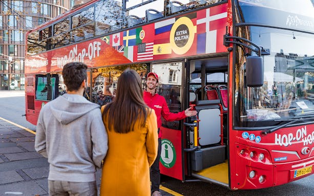 Tourists boarding a red Hop-On Hop-Off bus with guide in city center.