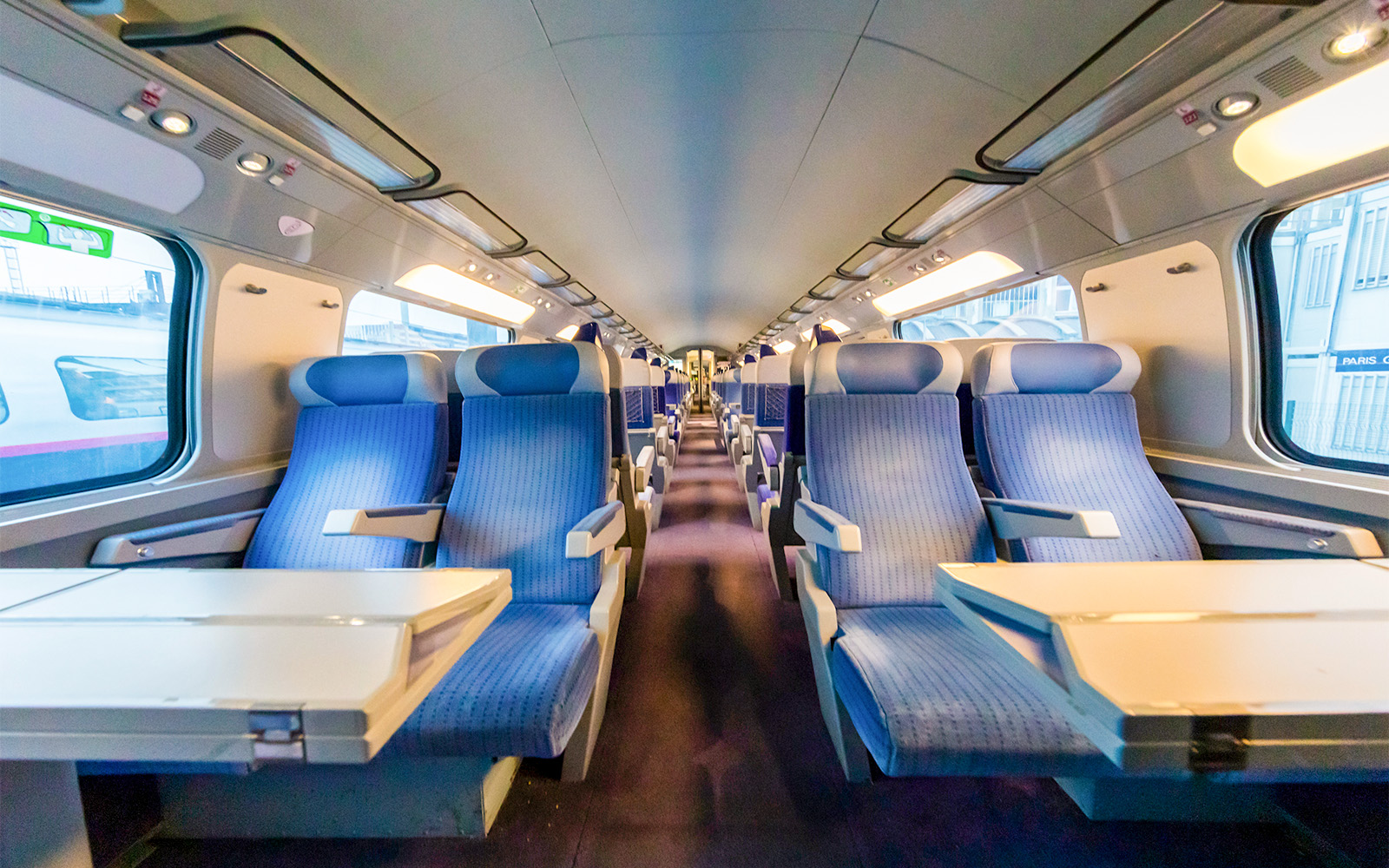 Train interior from Paris with blue seats and tables.