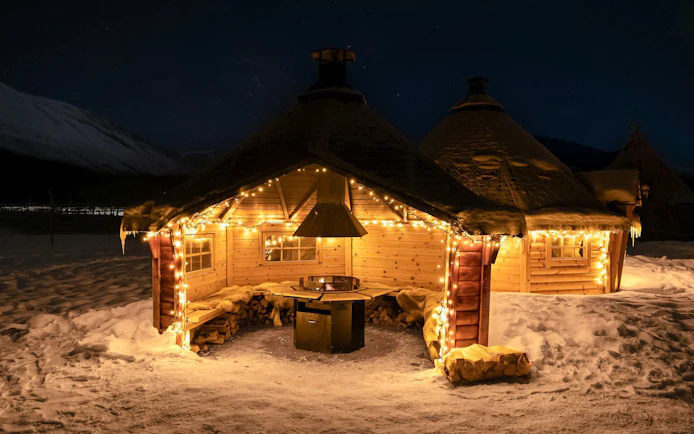 Cozy wooden cabin with lights in snowy Tromso, Norway, part of Northern Lights and Sami tour.