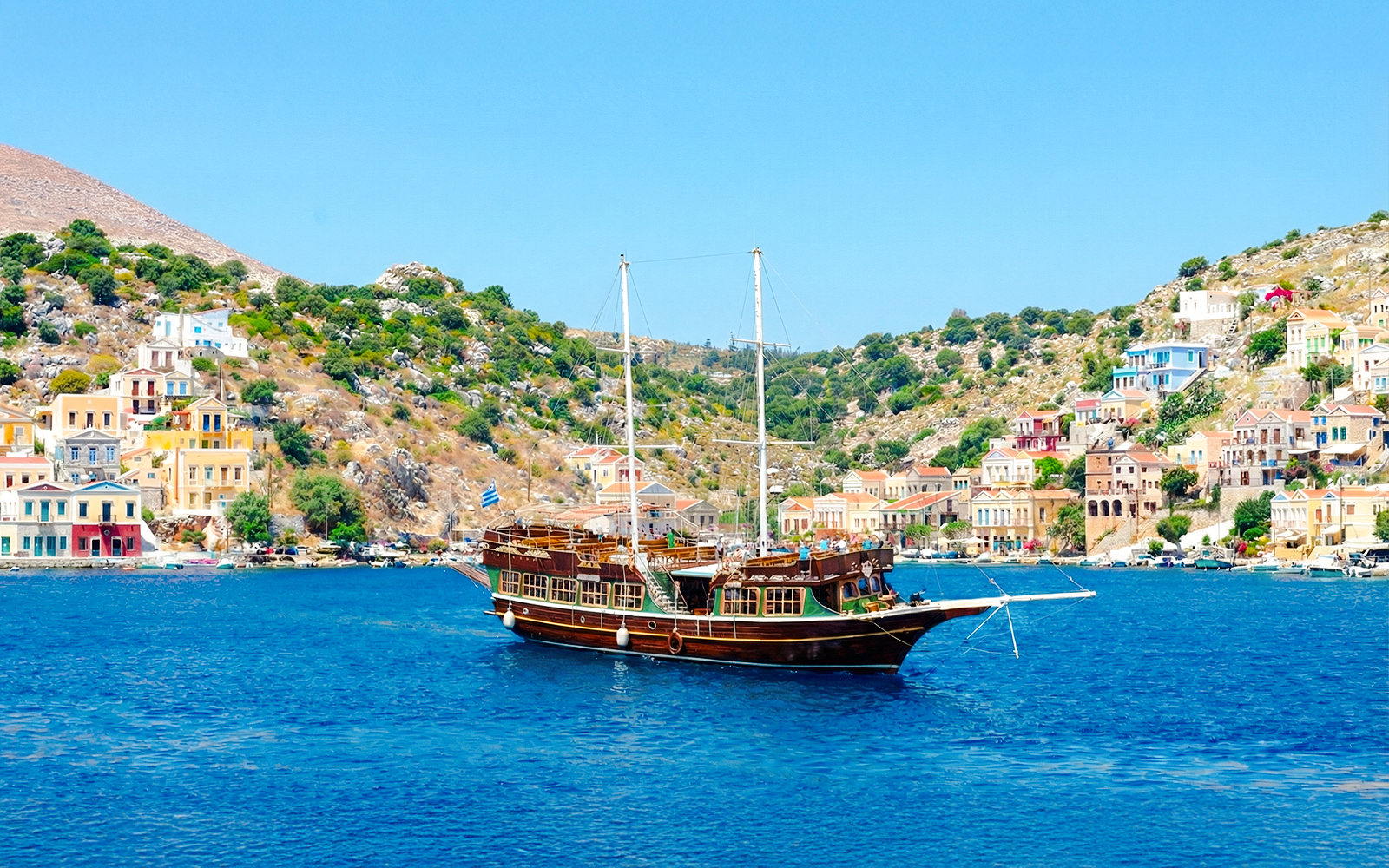 Sailing ship near colorful houses on a hillside, Rhodes day cruise.