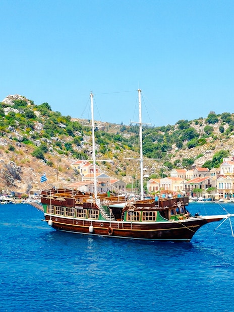 Sailing ship near colorful houses on a hillside, Rhodes day cruise.