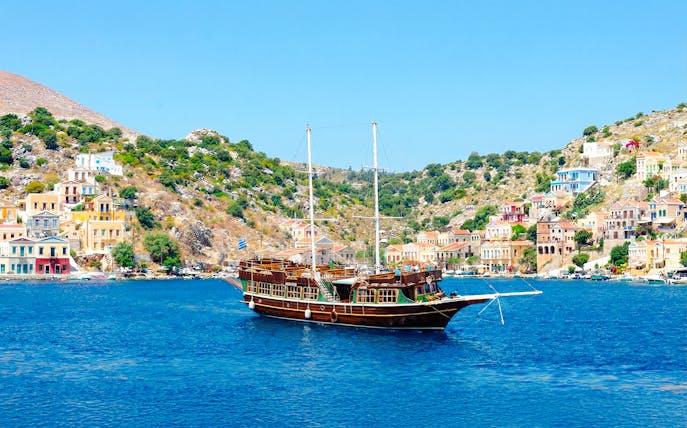Sailing ship near colorful houses on a hillside, Rhodes day cruise.