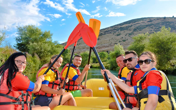 Group rafting on Bistrice River near Saranda, paddles raised, surrounded by lush greenery.
