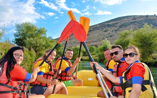 Group rafting on Bistrice River near Saranda, paddles raised, surrounded by lush greenery.