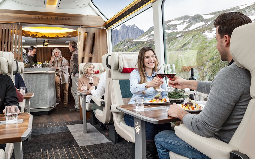 Passengers enjoying a meal and wine on a scenic Swiss train journey.