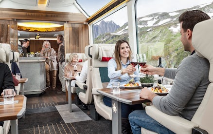 Passengers enjoying a meal and wine on a scenic Swiss train journey.