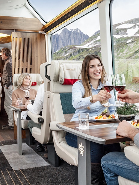 Passengers enjoying a meal and wine on a scenic Swiss train journey.