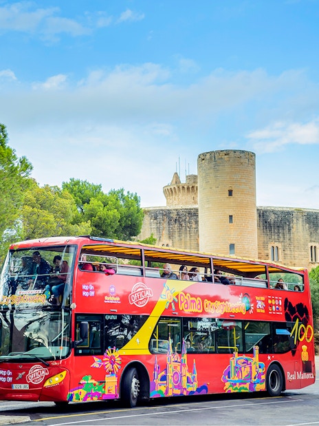 HOHO tour bus in front of Bellver Castle, Mallorca, surrounded by trees.