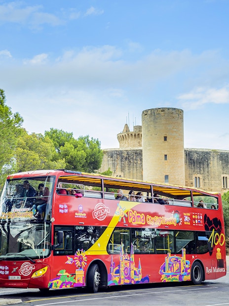 HOHO tour bus in front of Bellver Castle, Mallorca, surrounded by trees.