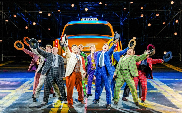 Performers in colorful suits holding hats in front of a taxi during "Guys & Dolls" on Sydney Harbour.