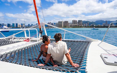 Couple relaxing on a catamaran net with Waikiki skyline in the background during whale watch sail.
