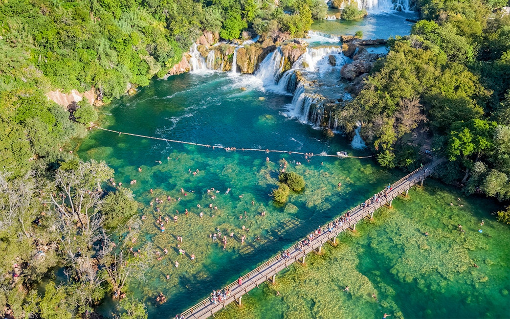 Aerial view of Krka waterfall and bridge with visitors swimming at Krka National Park, Croatia.