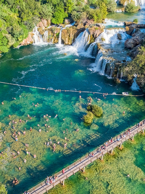 Aerial view of Krka waterfall and bridge with visitors swimming at Krka National Park, Croatia.