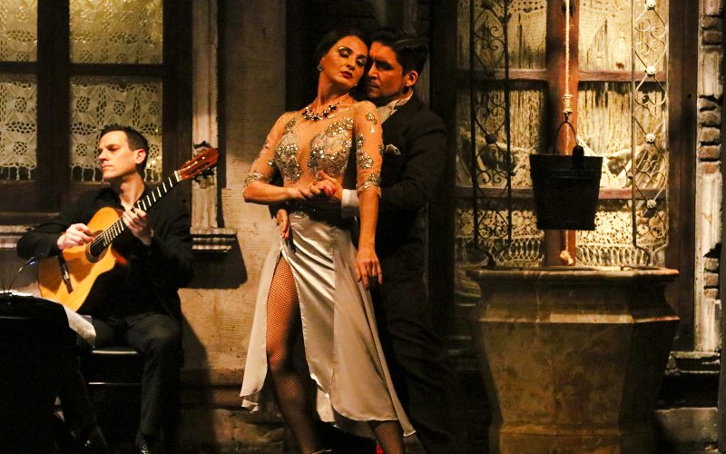 Tango dancers performing at Aljibe Tango Show in Buenos Aires with guitarist in background.