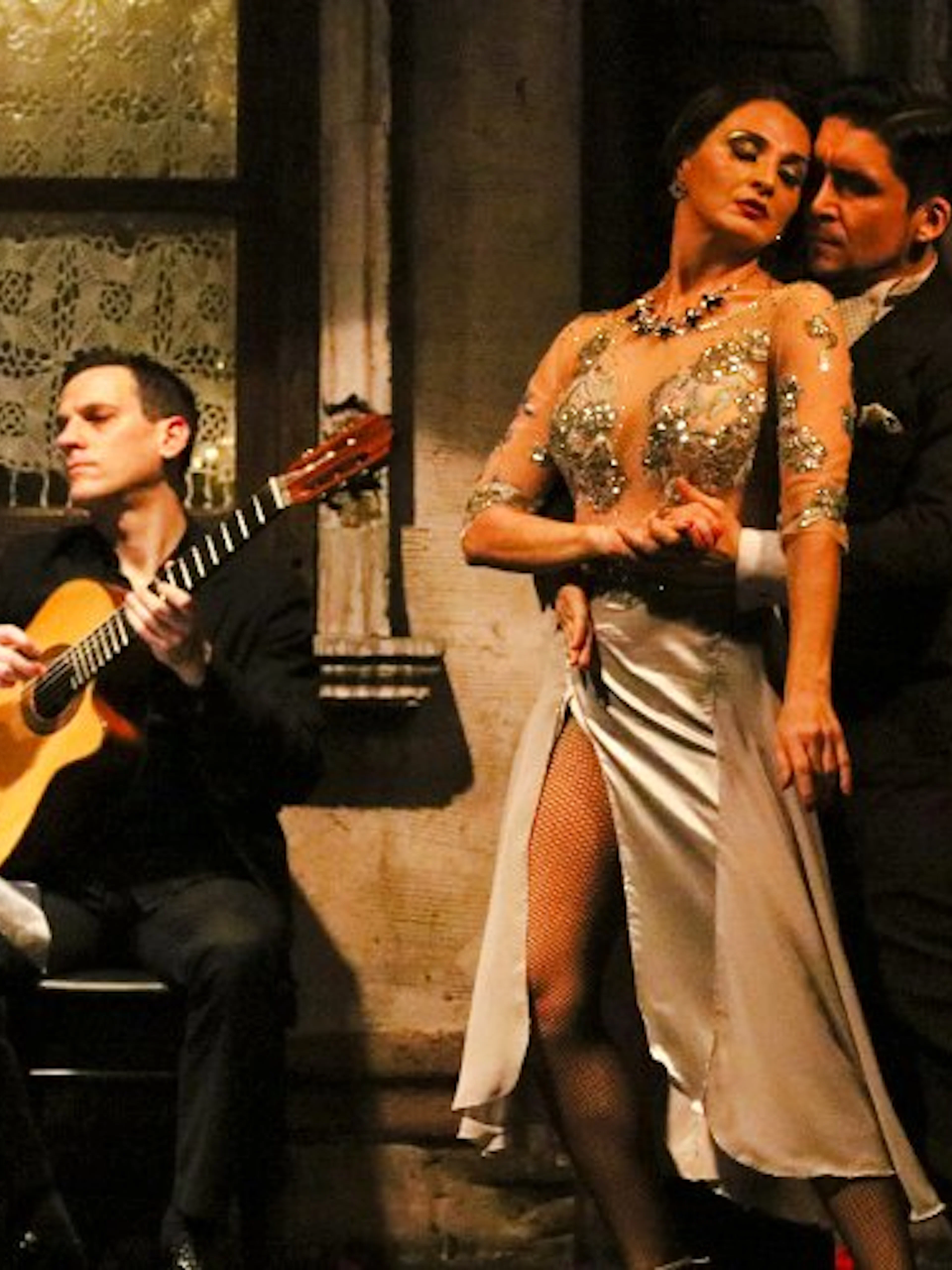 Tango dancers performing at Aljibe Tango Show in Buenos Aires with guitarist in background.