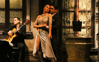 Tango dancers performing at Aljibe Tango Show in Buenos Aires with guitarist in background.
