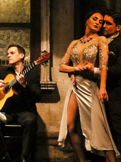 Tango dancers performing at Aljibe Tango Show in Buenos Aires with guitarist in background.